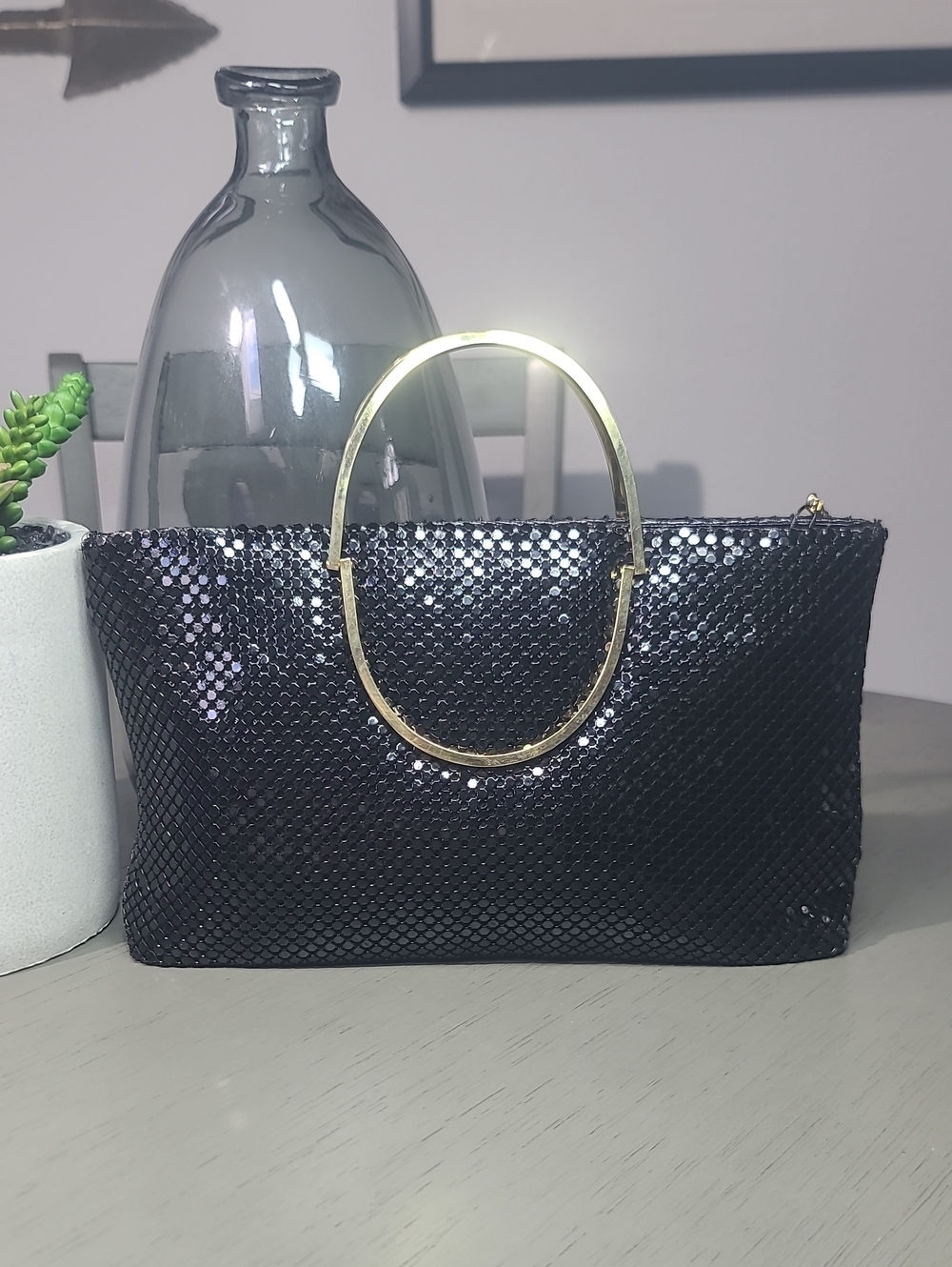 Sophisticated black mesh metal  clutch with a polished gold-tone oval handle.